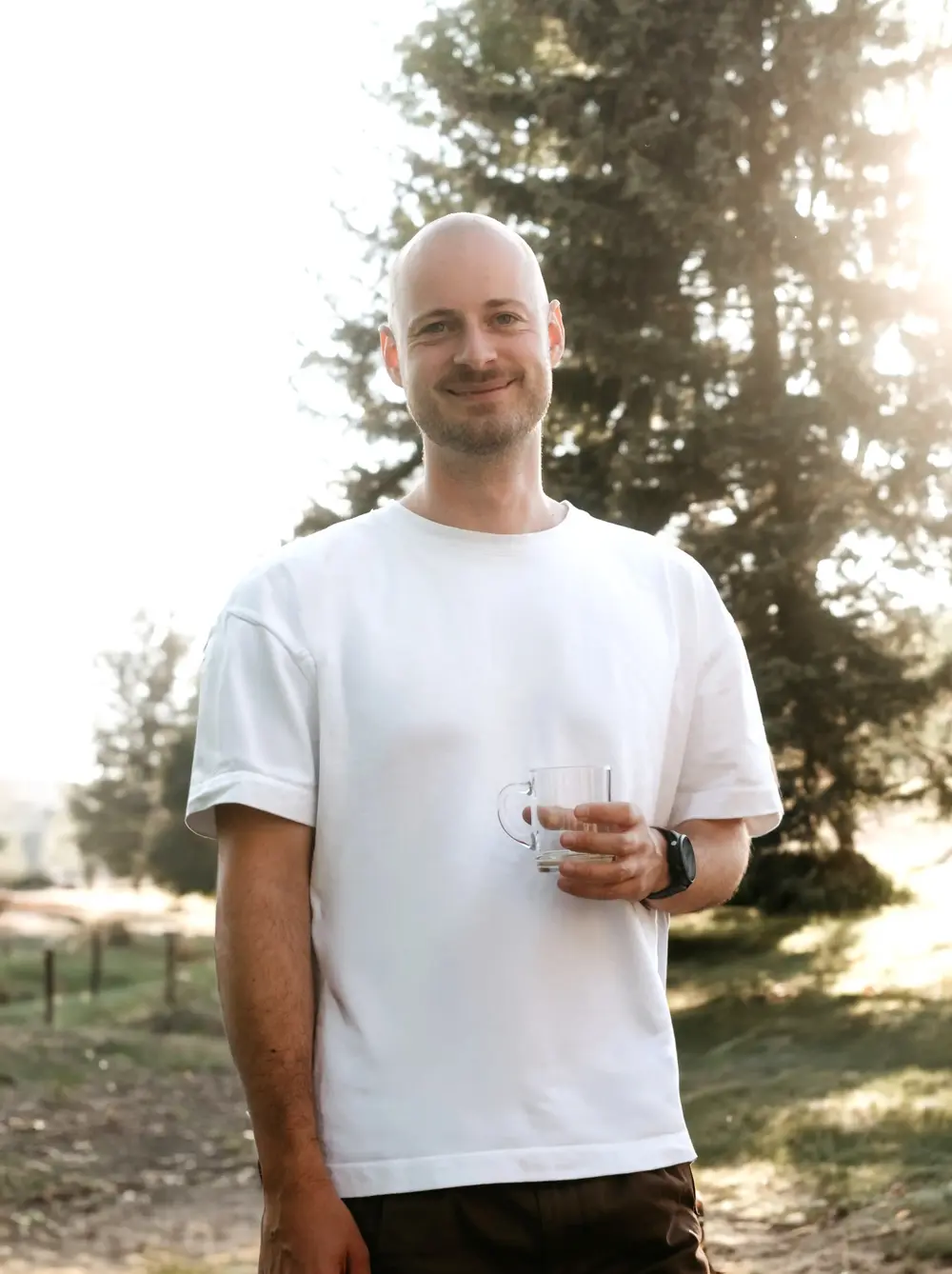 Fabian Zierer im weißen T-Shirt draußen im Abendlicht, ein Glas in der Hand