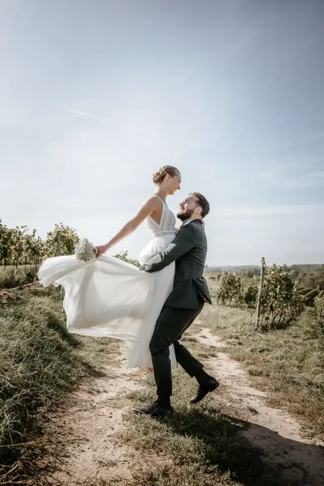 Bräutigam hebt die Braut im Weinberg hoch, ihr Kleid fliegt